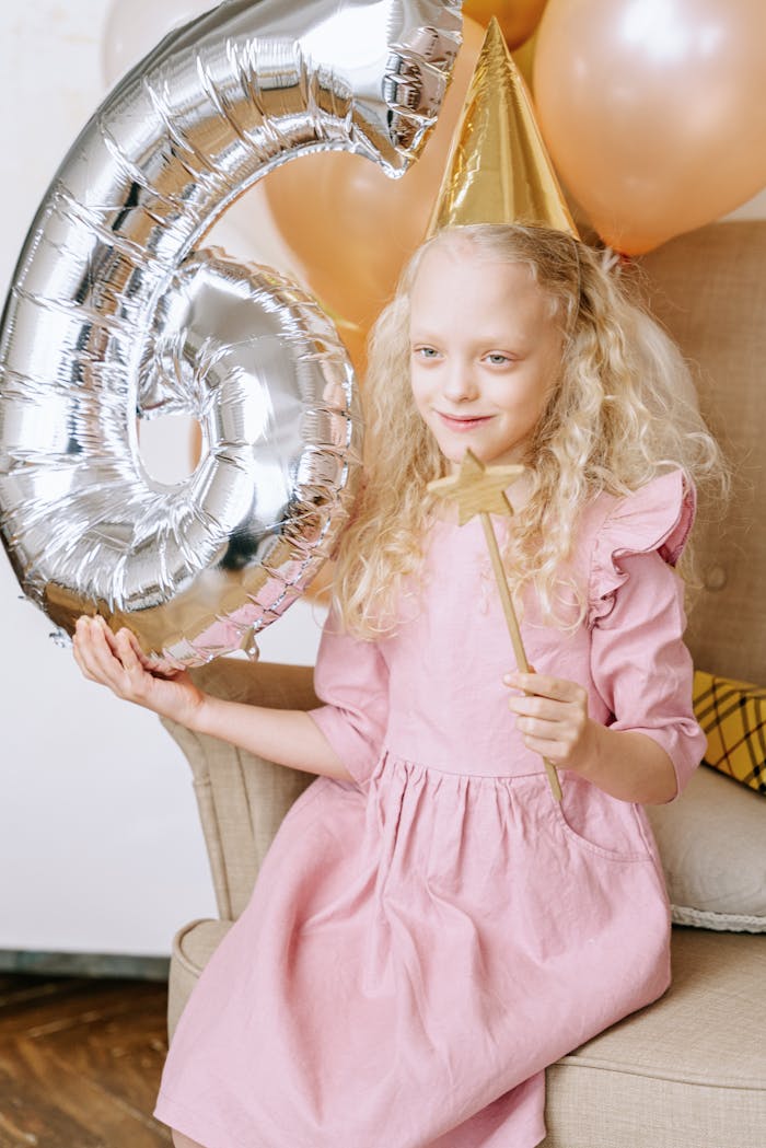 Adorable girl celebrating her birthday with a number six balloon and party hat